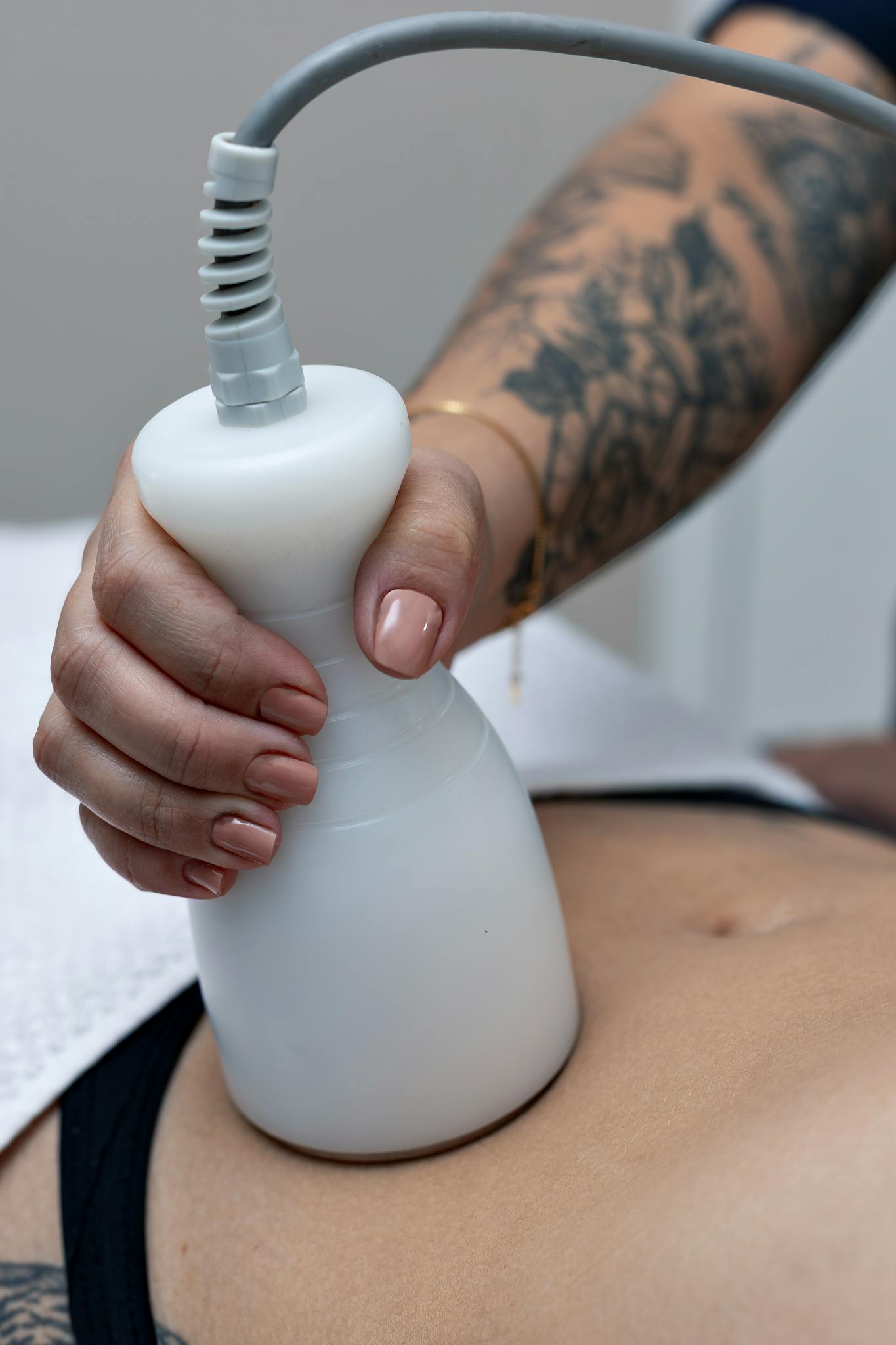 A tattooed therapist performs a body contouring procedure on a client's abdomen in Belo Horizonte.